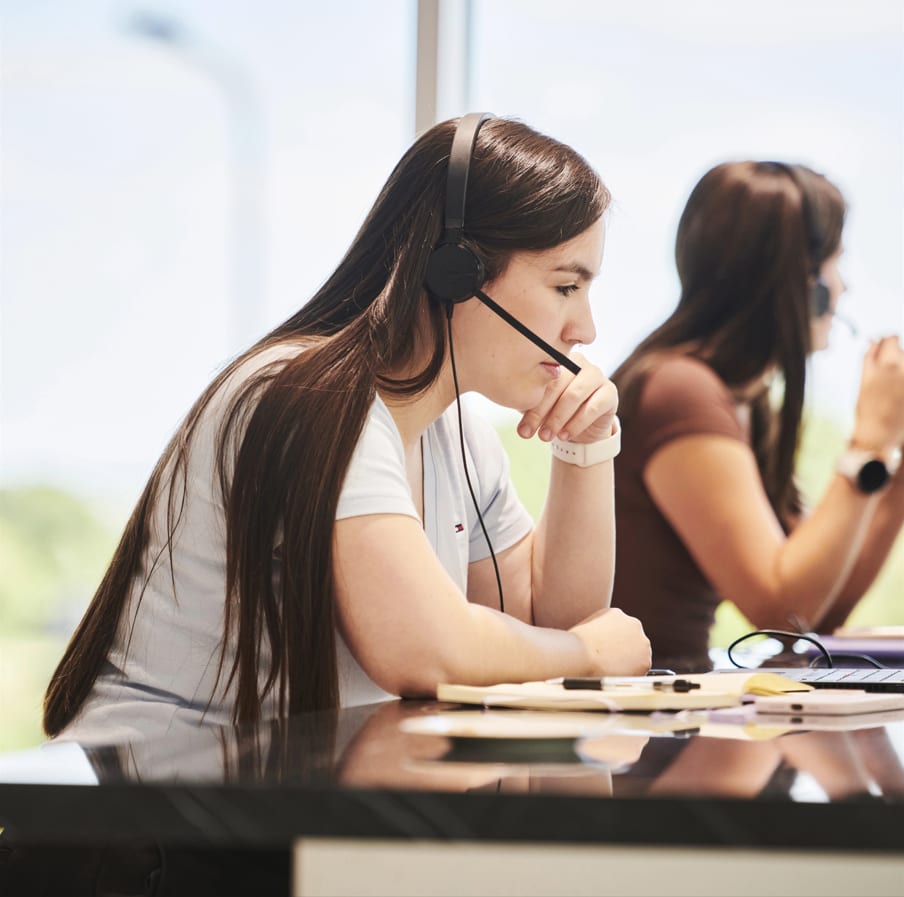 A young woman on a phone call using a headset sat at a desk
