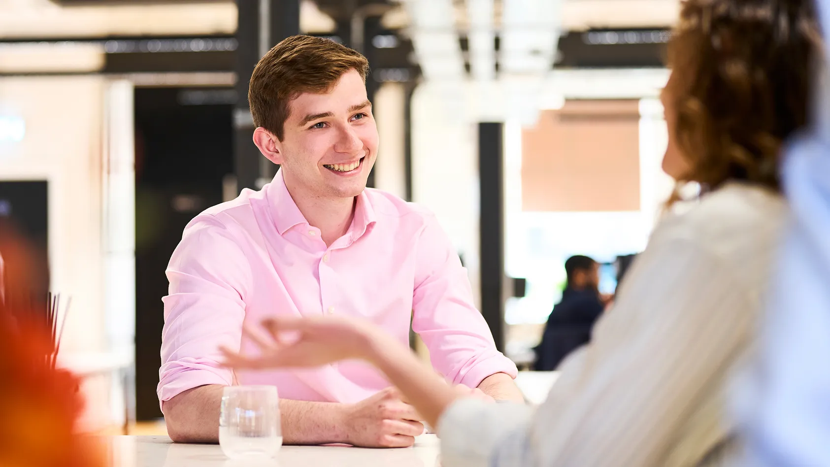 A young man in a pink shirt smiling and engaging in conversation.