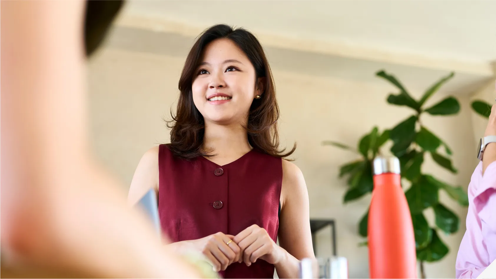 A young woman wearing a maroon top, smiling and engaging in conversation indoors.