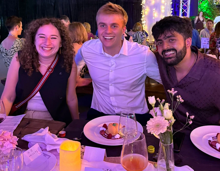 Three colleagues sat together at a dining table, smiling.